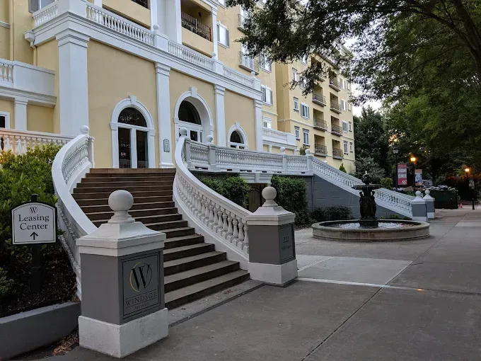 Curved staircase leading to a yellow building entrance with arched windows and trees along the sidewalk