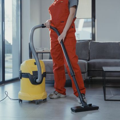 A woman in red overalls is using a yellow vacuum cleaner in a living room