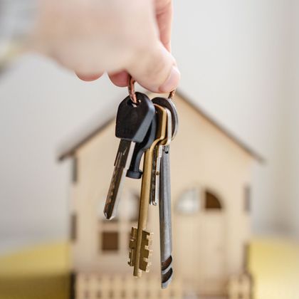 A person is holding a bunch of keys in front of a model house.