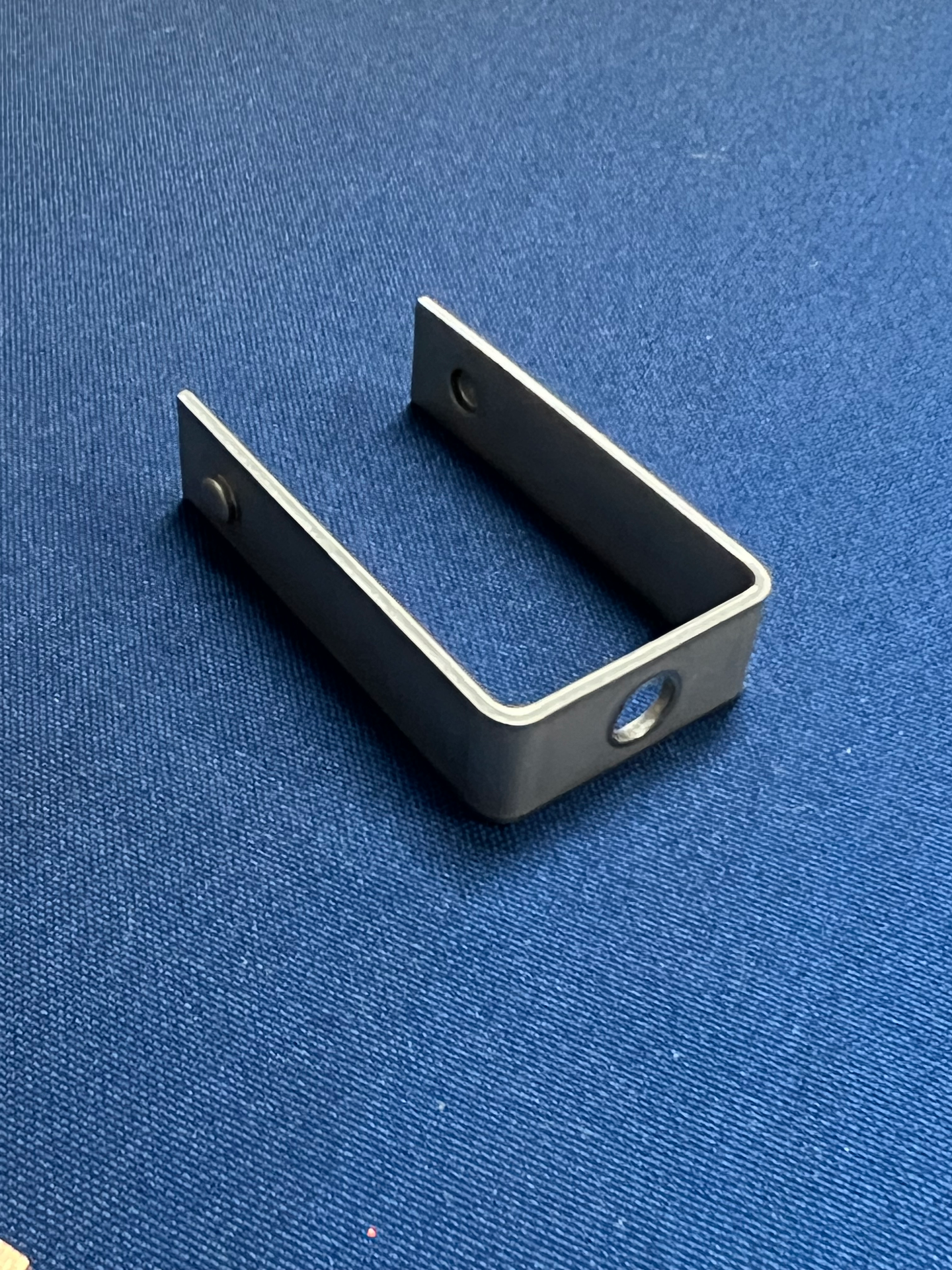 A metal bracket with a hole in the middle is sitting on a blue cloth.