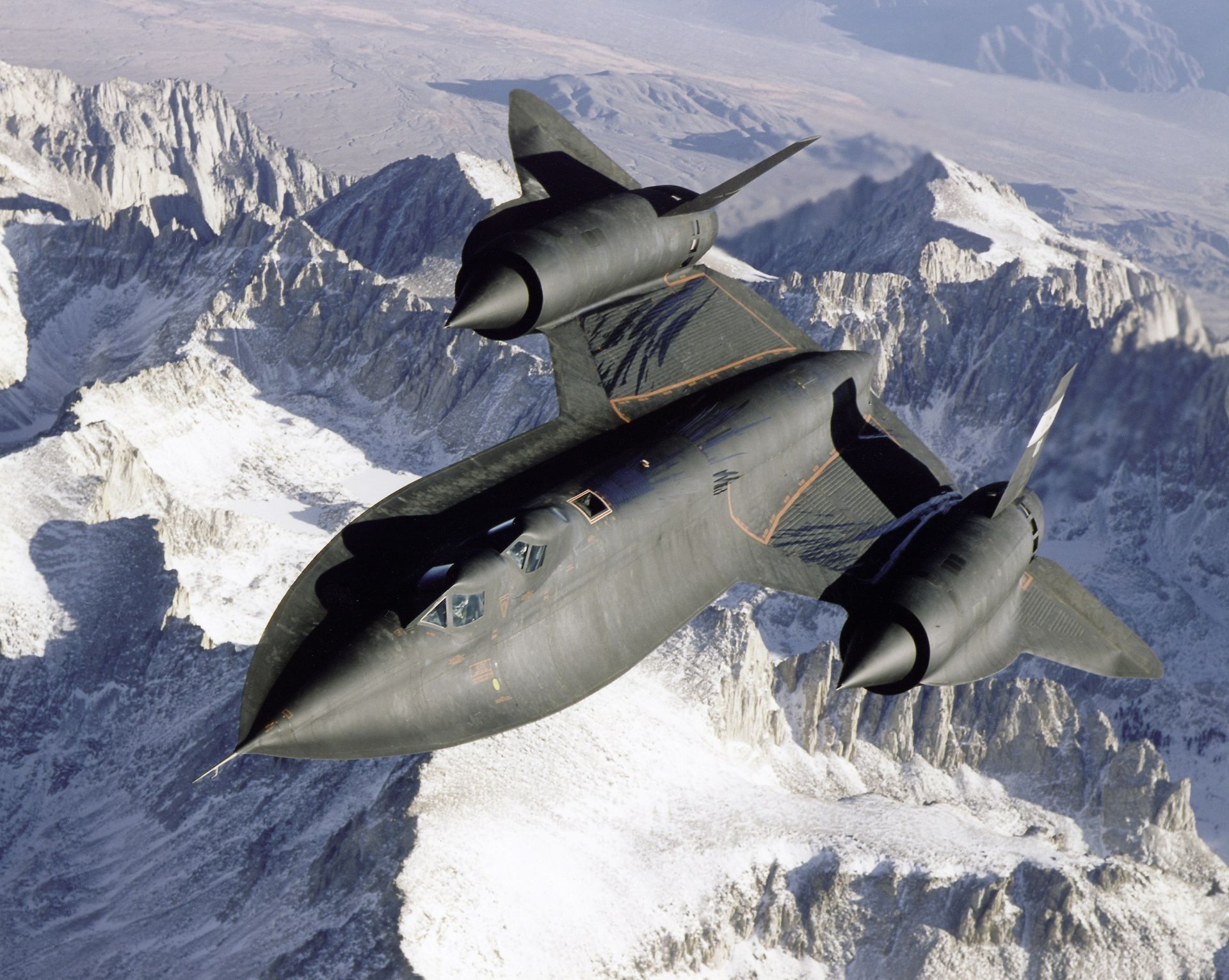 A black jet is flying over a snowy mountain range