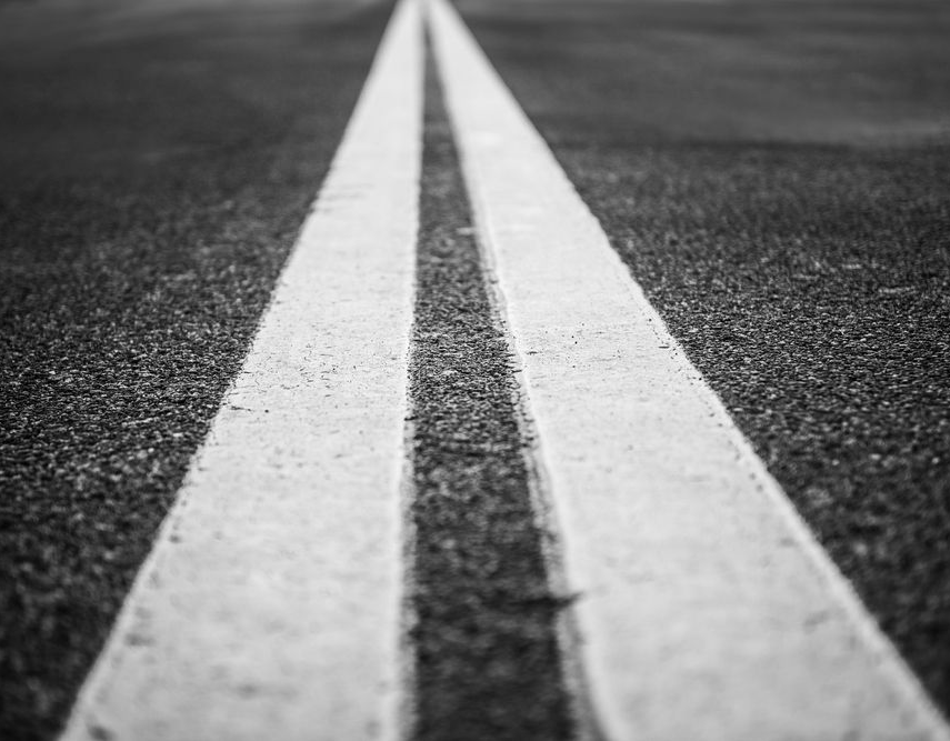 Double yellow lines on an asphalt road, viewed from a low angle.