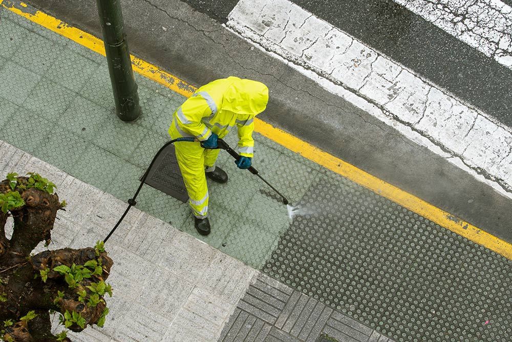 A Man in a Yellow Suit is Cleaning the Sidewalk With a High Pressure Washer — North Coast Line Marking in Gold Coast, NSW