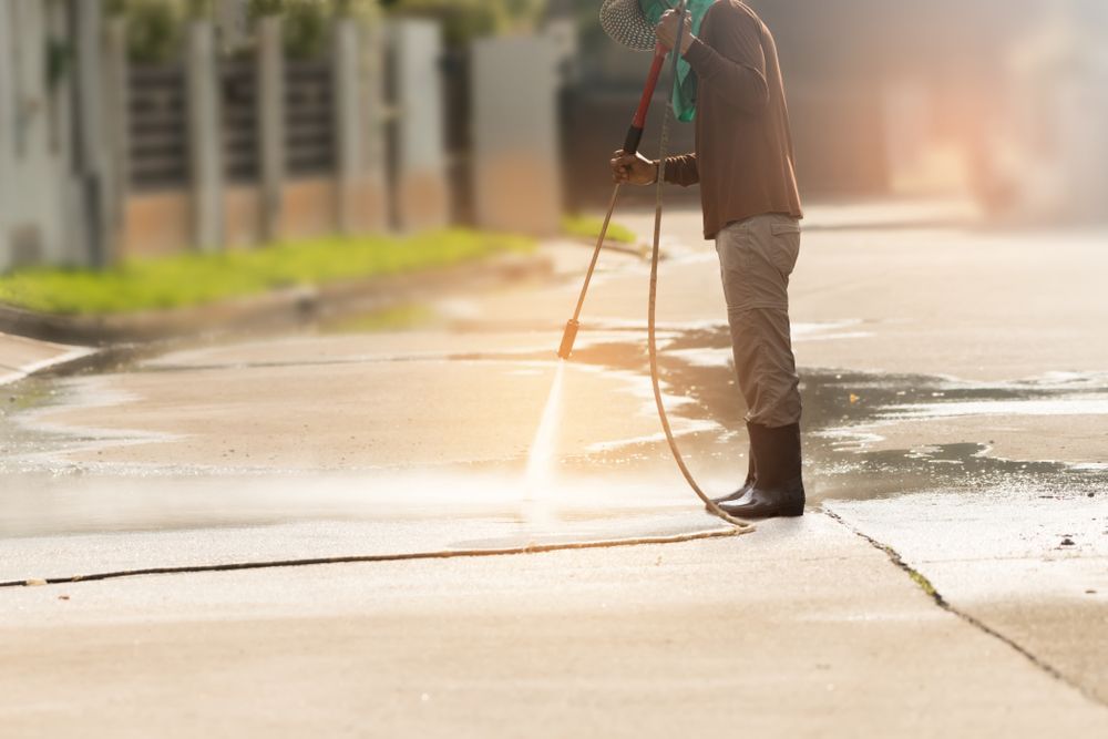 A Man is Cleaning the Sidewalk With a High Pressure Washer — North Coast Line Marking in Talofa, NSW