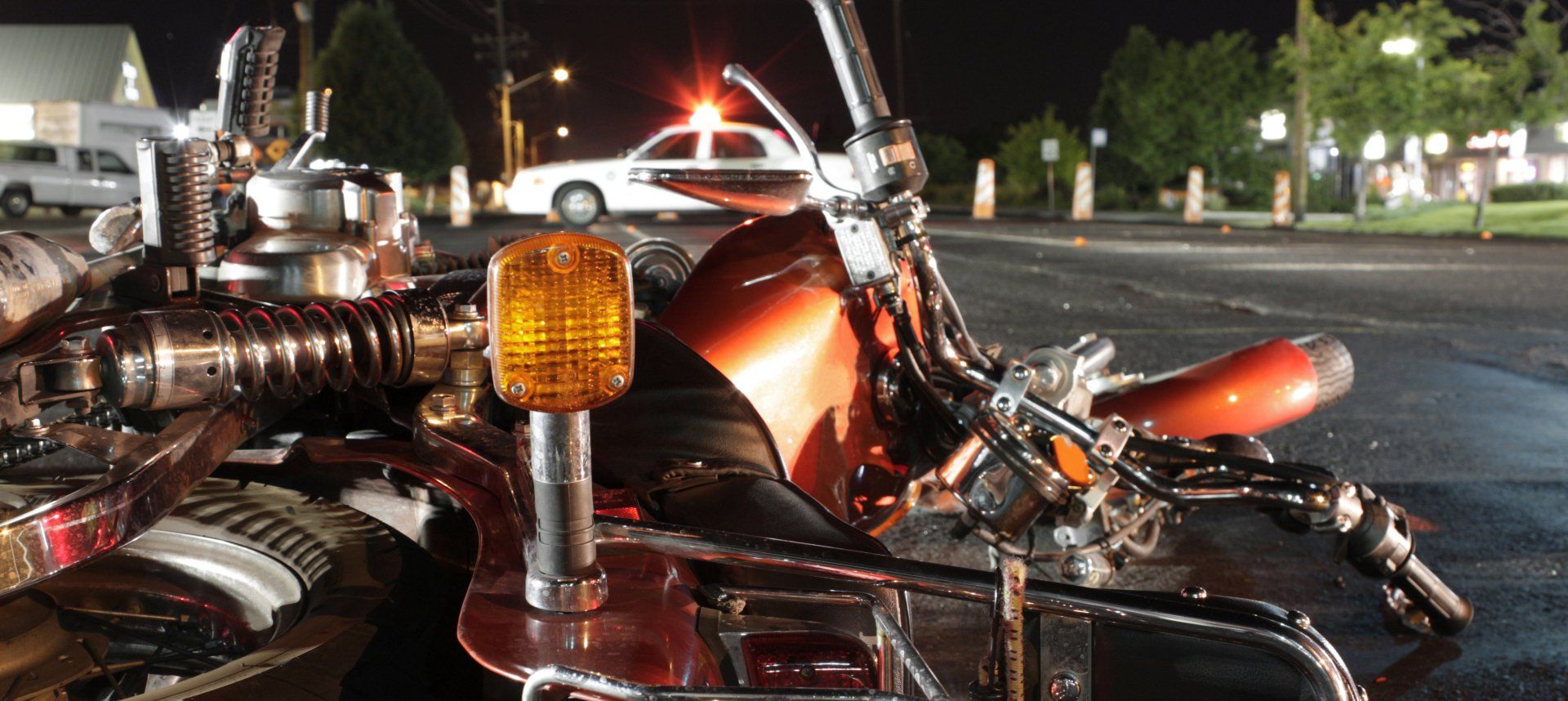 Motorcycle wreck at night, orange turn signal, police car with lights on in the background.
