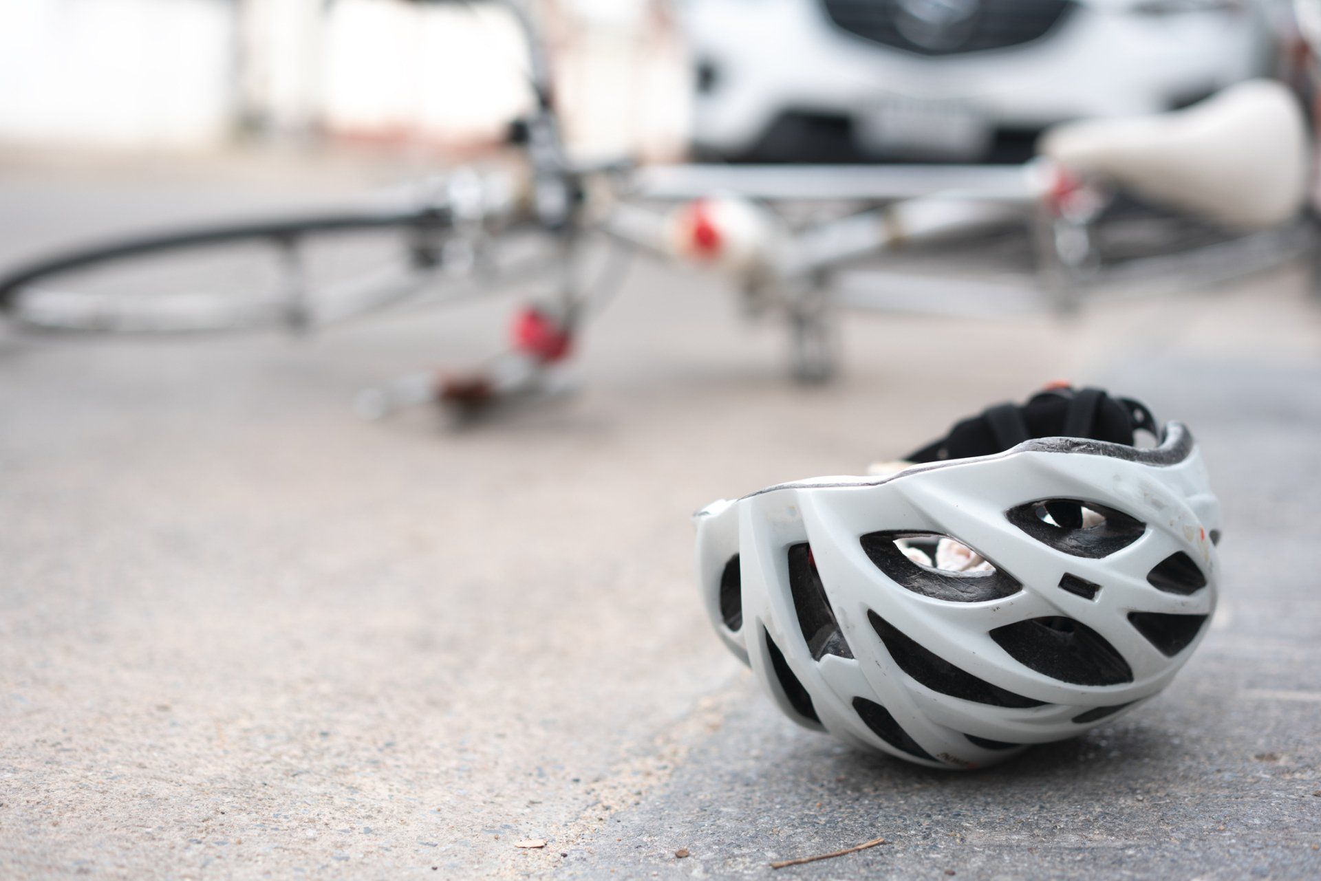 White bicycle helmet on pavement, bike and car blurred in the background.