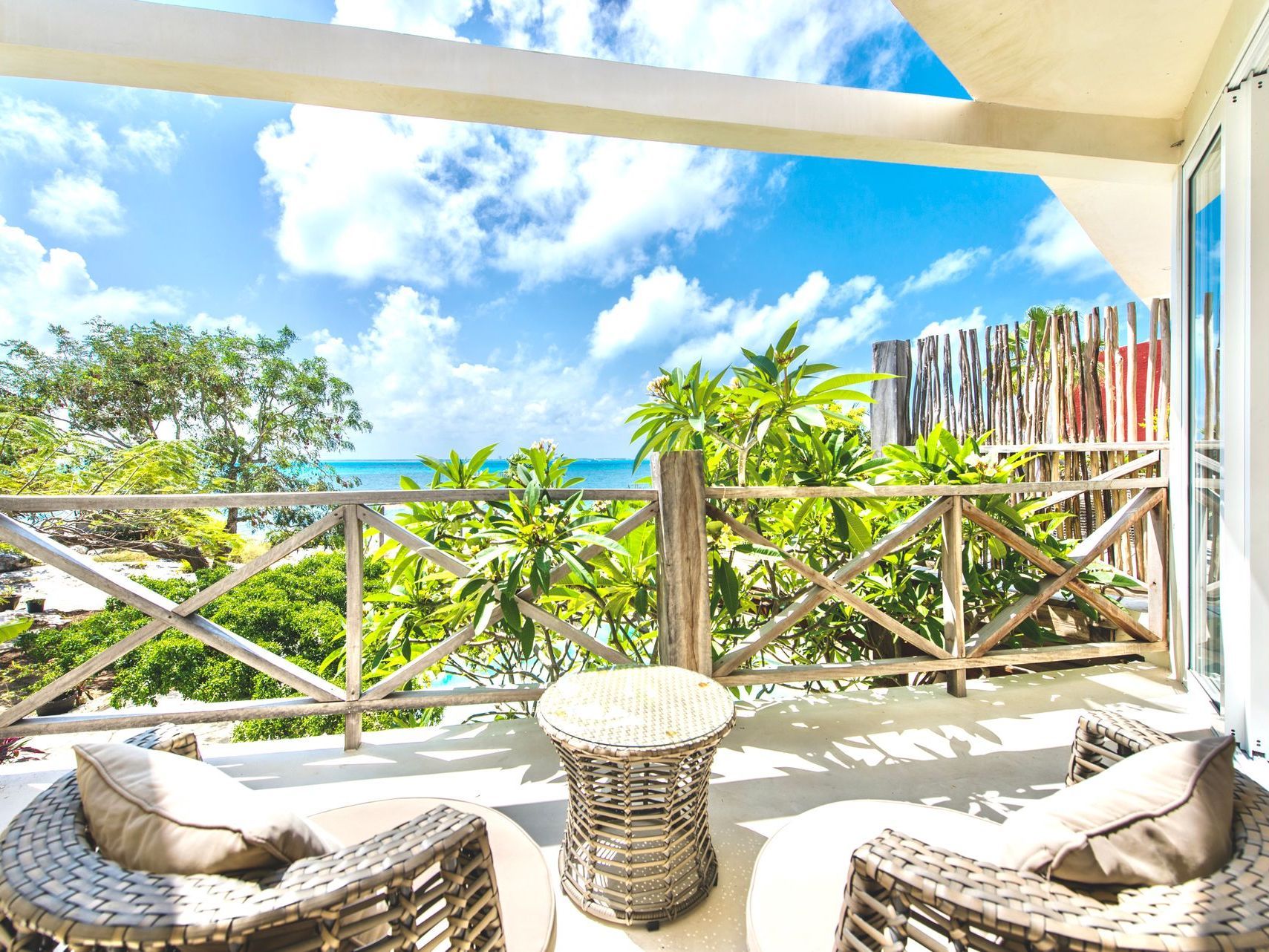 Balcony with woven chairs, wooden railing, and ocean view on a sunny day.