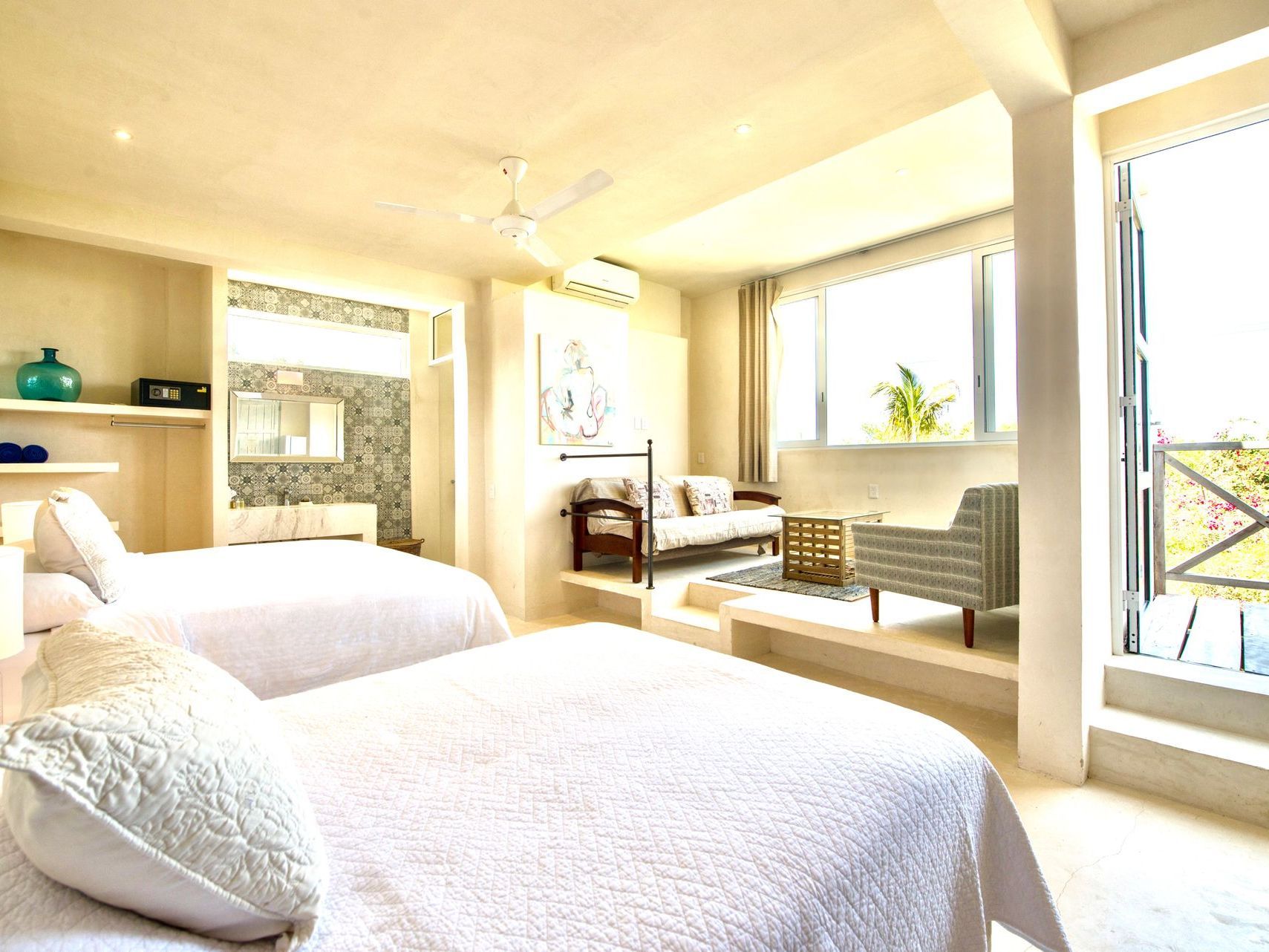 Bright hotel room with two beds, seating area, and balcony.
