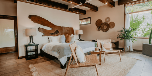 A bedroom with a bed , chairs , lamps and a large wooden sculpture on the wall.