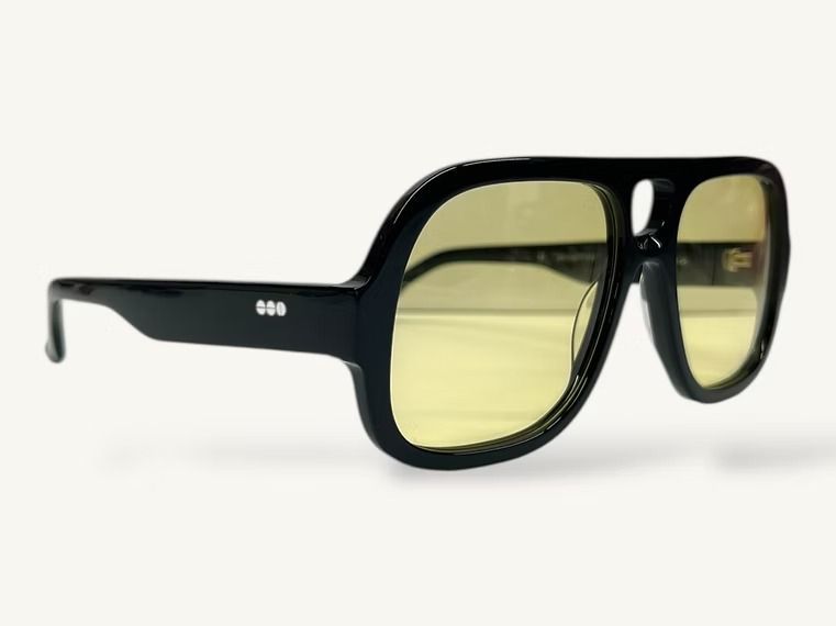 Occhiali da sole rettangolari neri con lenti color giallo su sfondo bianco.