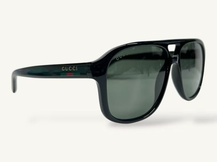 Occhiali da sole Gucci neri con lenti verdi su sfondo bianco.