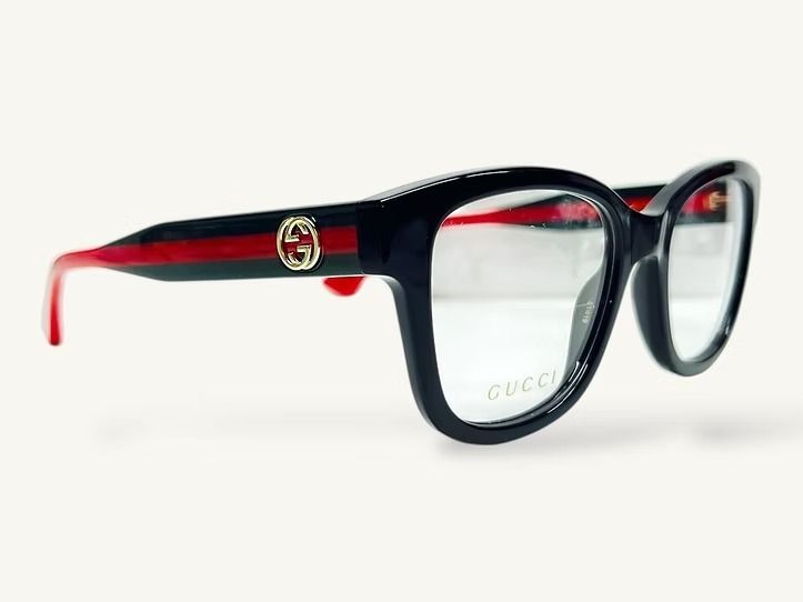 Occhiali da vista rettangolari neri con aste rosse e logo dorato su sfondo bianco.