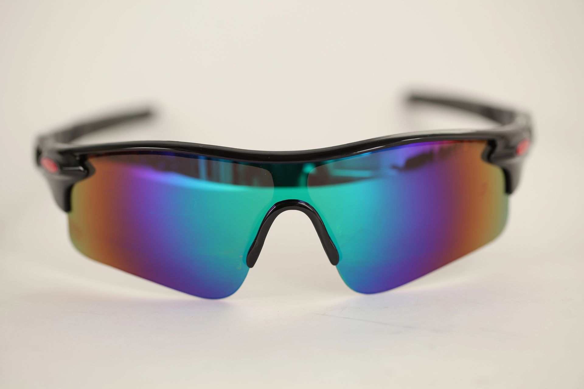 Occhiali da sole sportivi riflettenti con effetto arcobaleno e montatura nera su sfondo chiaro.