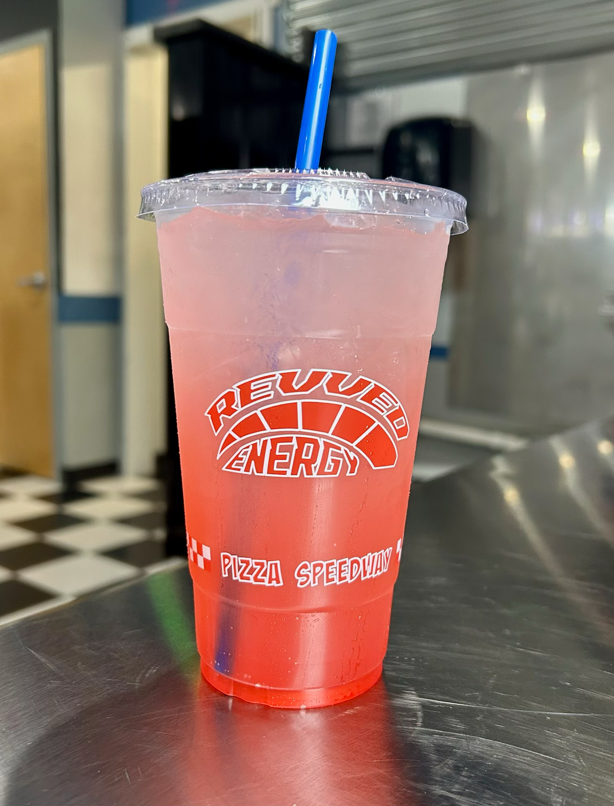 A cup of red liquid with a blue straw on a table.