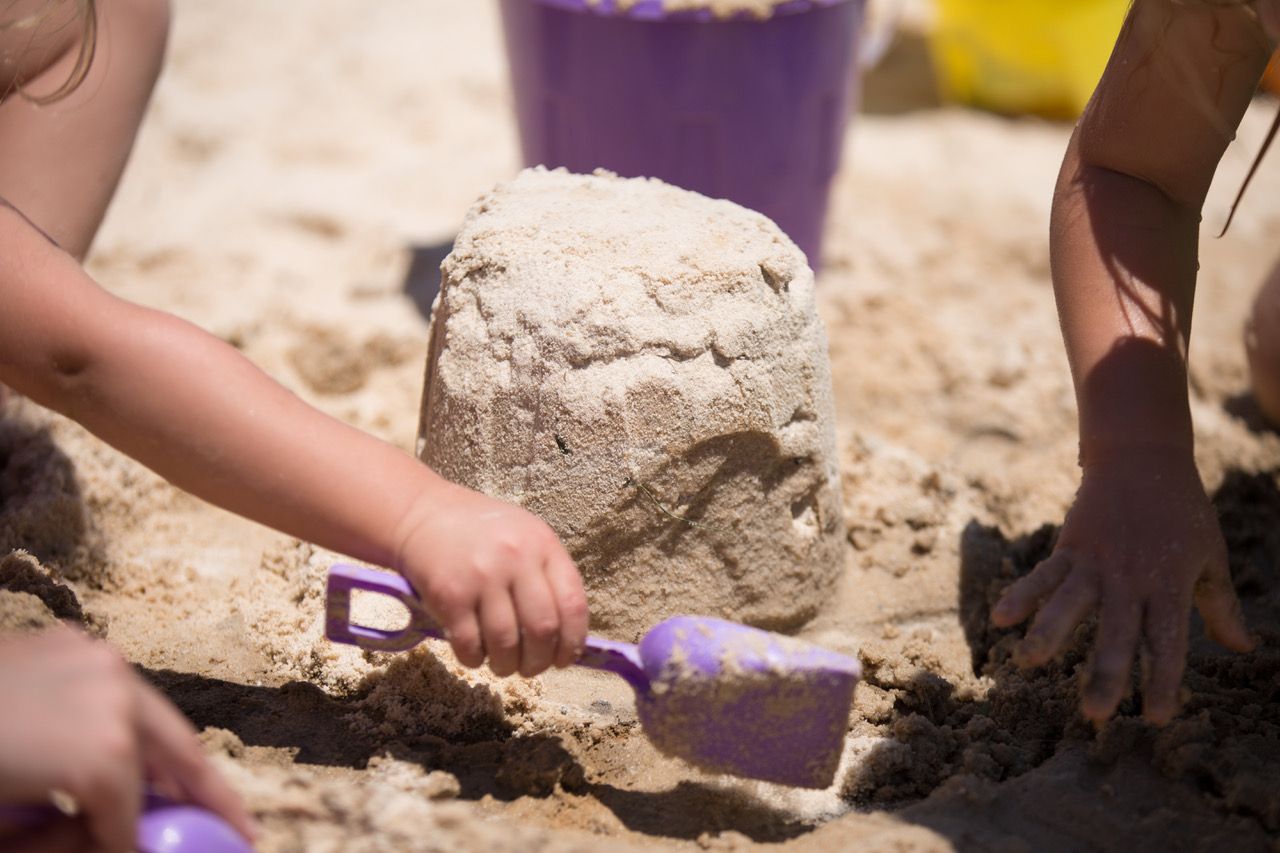 Two children are playing in the sand on the beach.