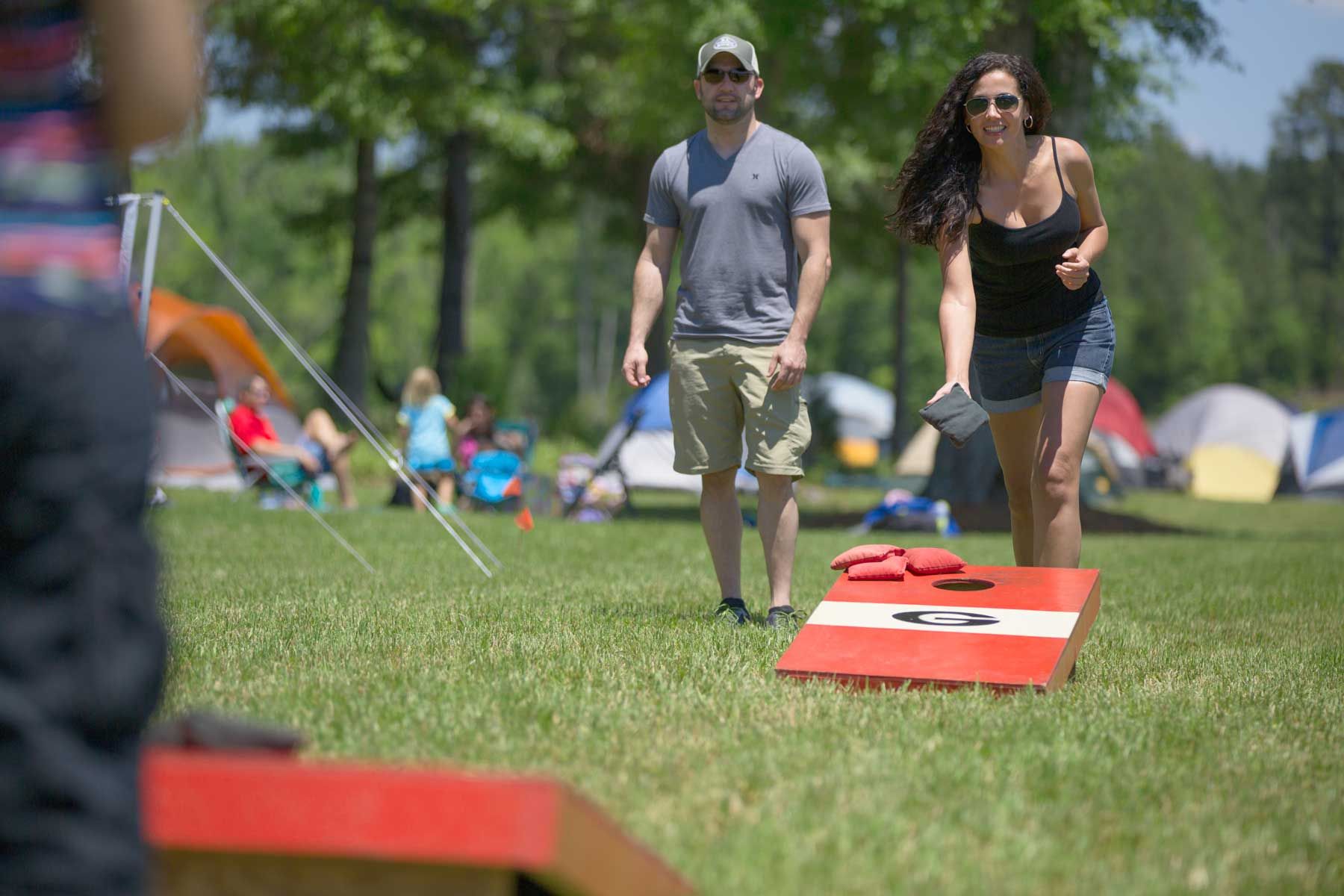 A man and a woman are playing cornhole in a park.