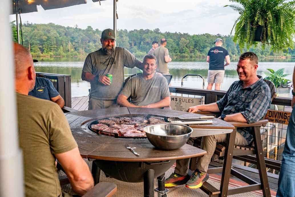 A group of men are sitting around a table with a grill.