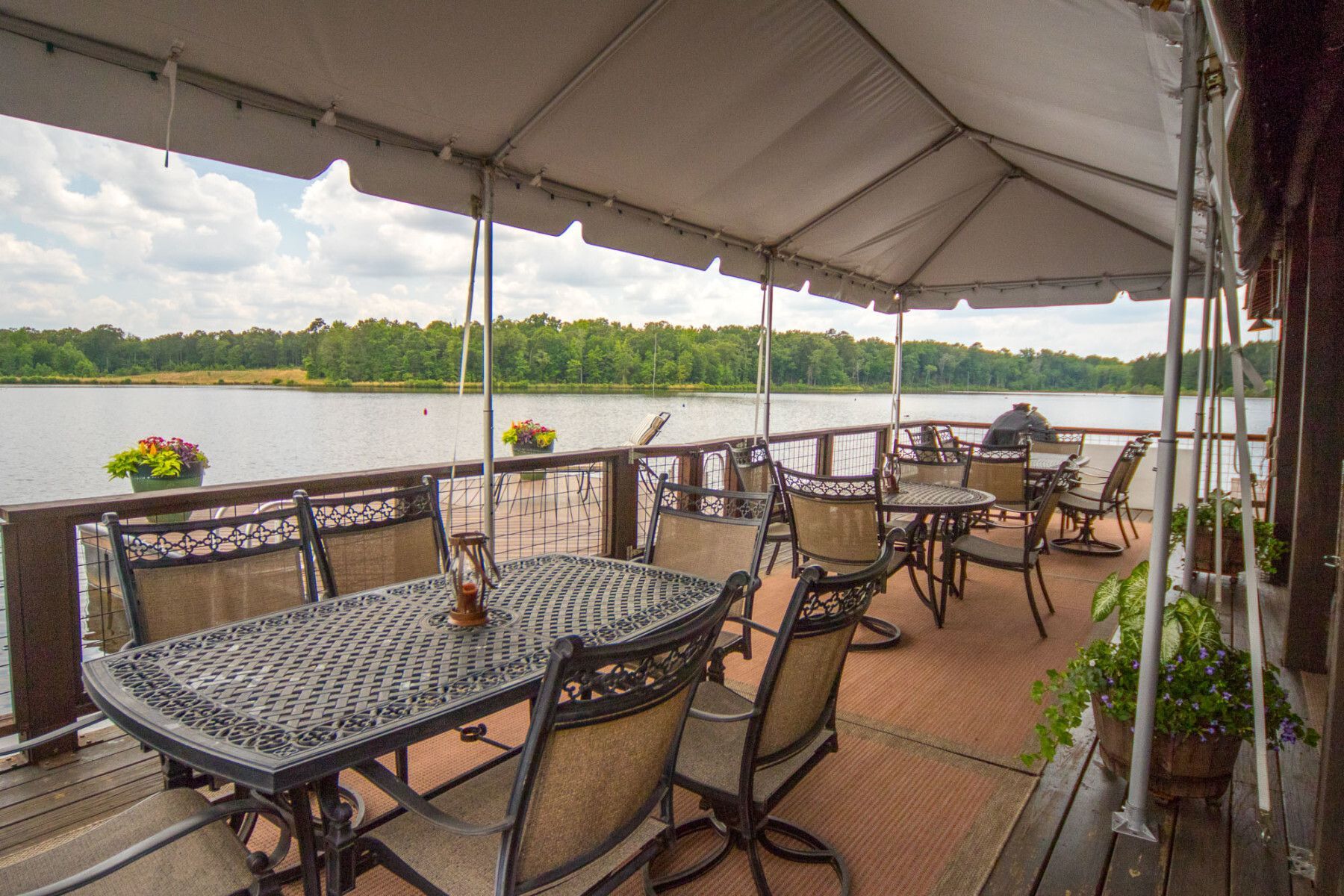 A patio with tables and chairs under a tent overlooking a lake.