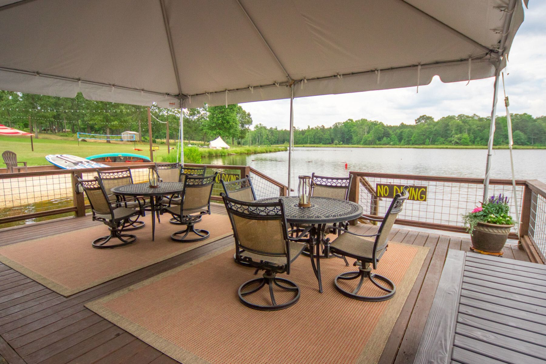 A patio with tables and chairs under a tent overlooking a lake.