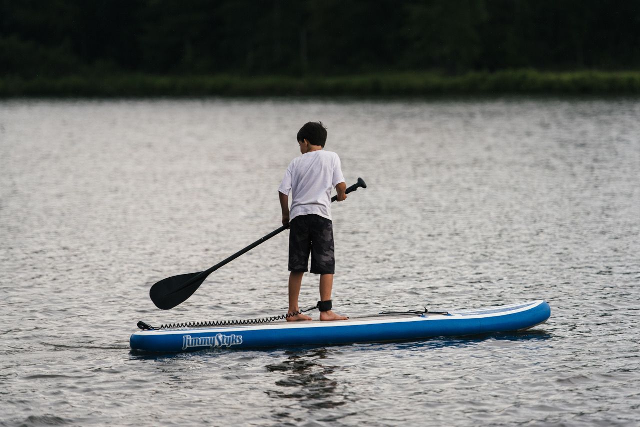 A young boy is riding a paddle board on a lake.