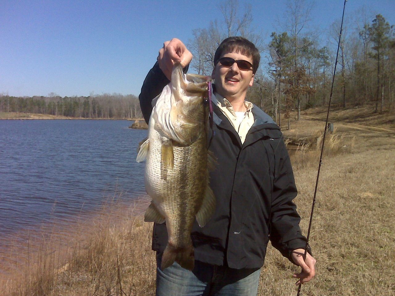 A man is holding a large fish in his hand in front of a lake