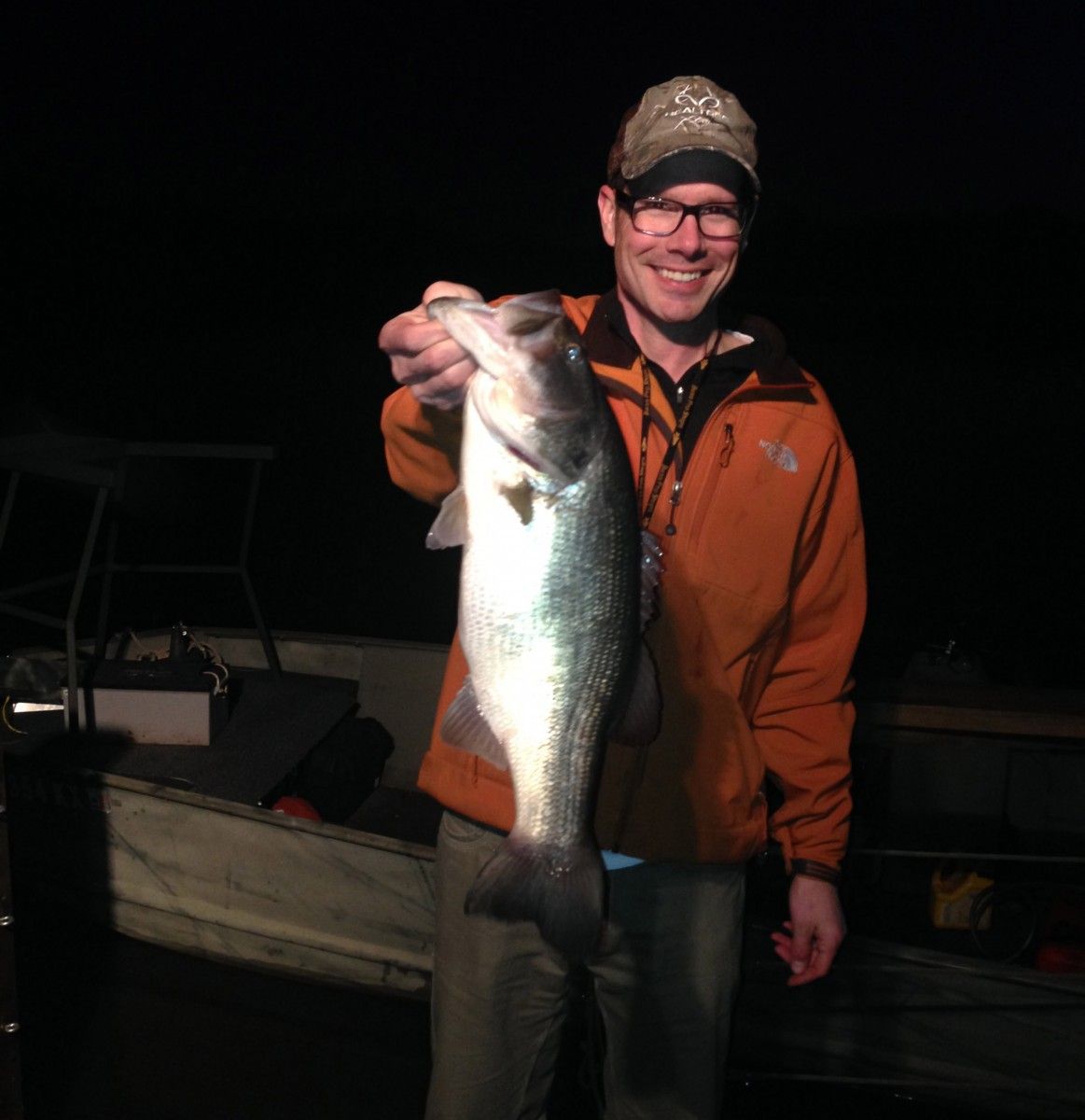 A man in an orange jacket is holding a large fish