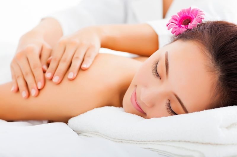Woman receiving a back massage in a spa. She has a pink flower in her hair and smiles.