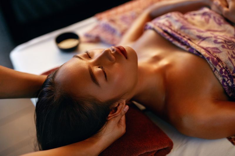 Woman receiving head massage at spa; eyes closed, relaxed expression.