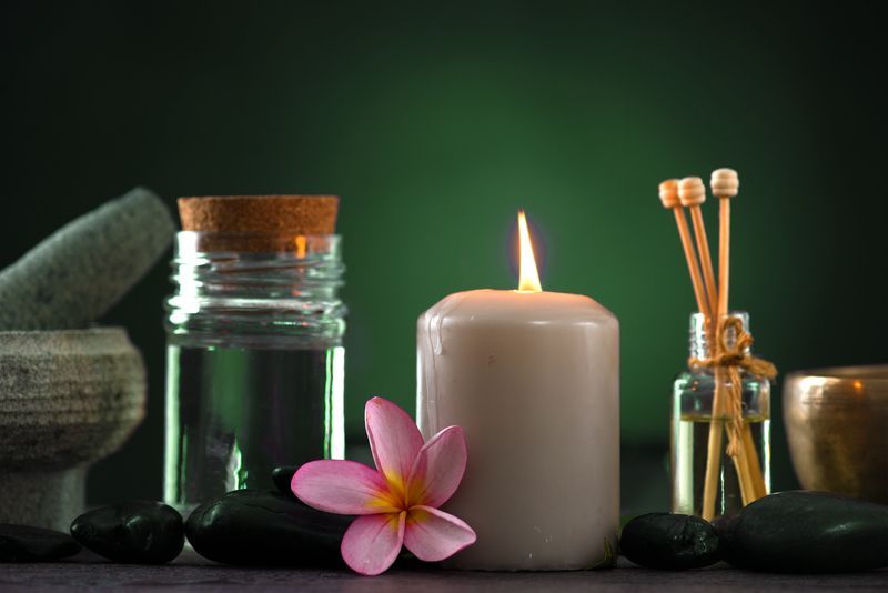 Candle, essential oils, and flower on black stones, with a green background.