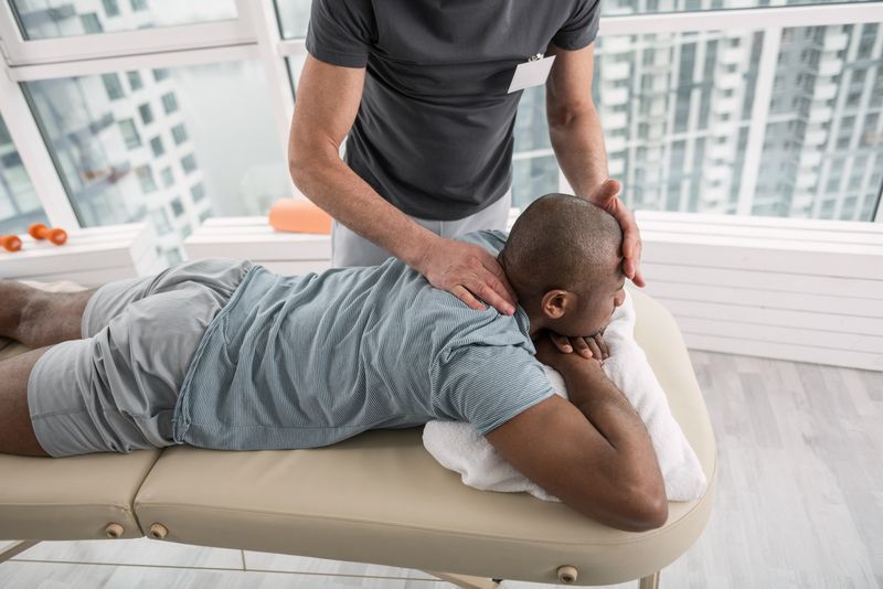Man receiving neck massage on a massage table by a person wearing a grey shirt.