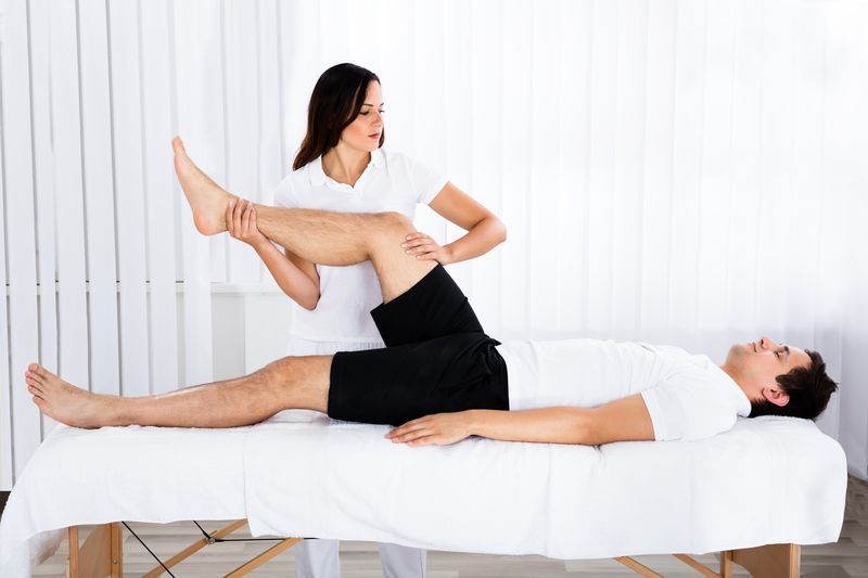 Physical therapist stretching a patient's leg on a treatment table.