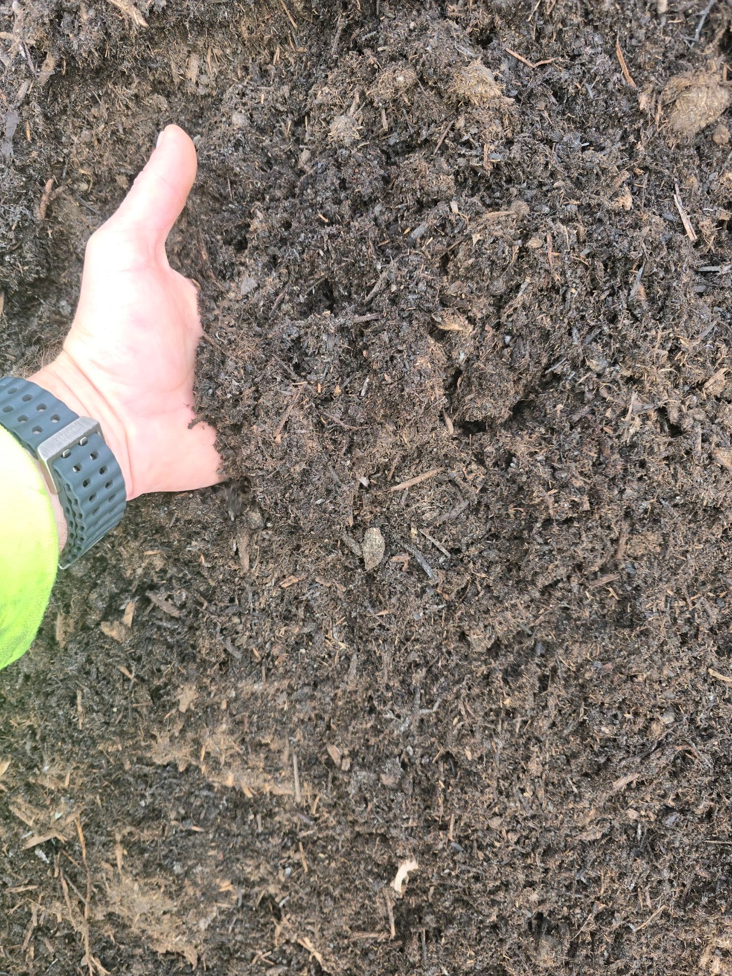 Hand holding a clump of dark, crumbly soil against a background of more soil.