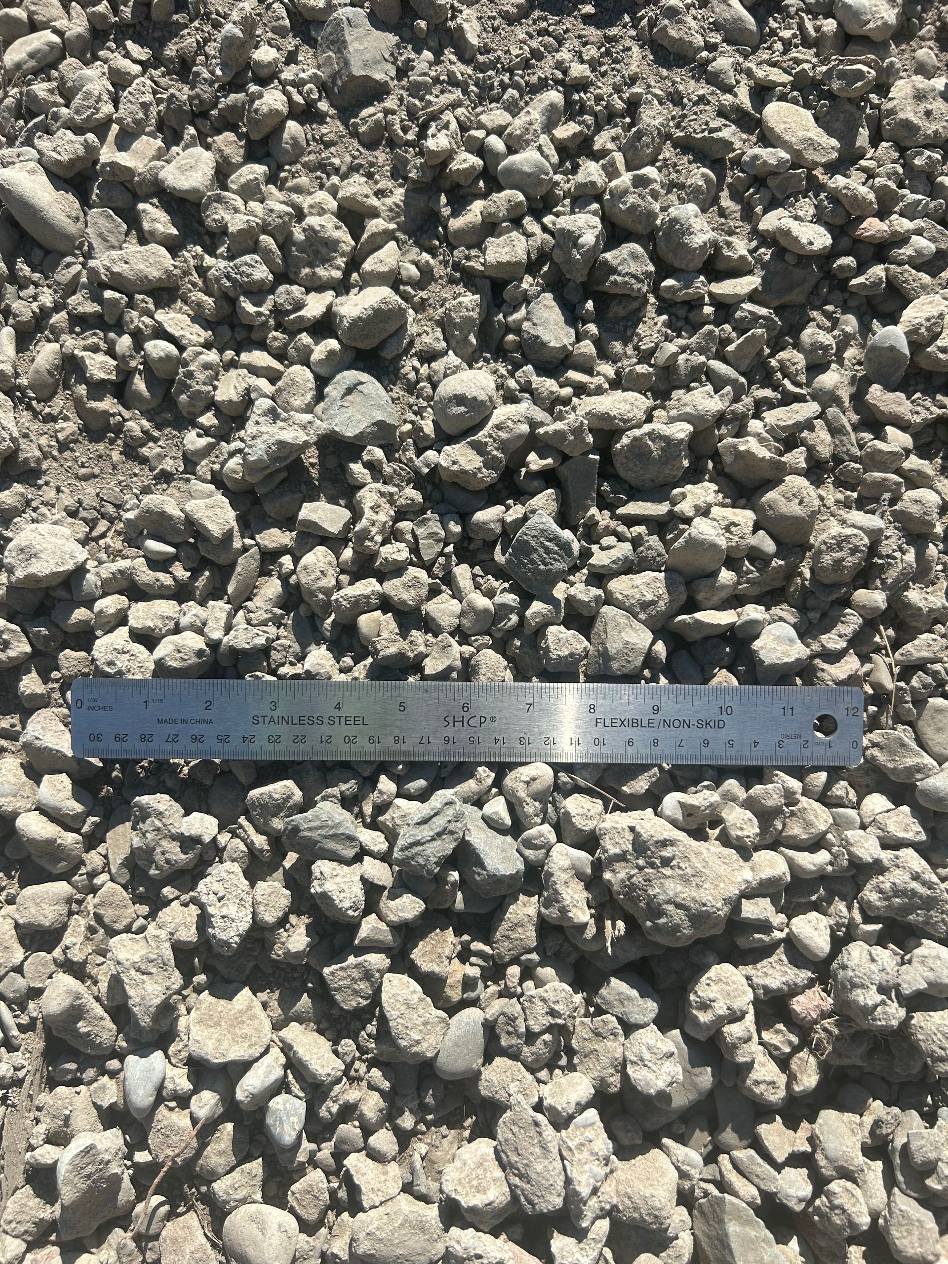 Gravel pile with a ruler for scale; gray and tan rocks.