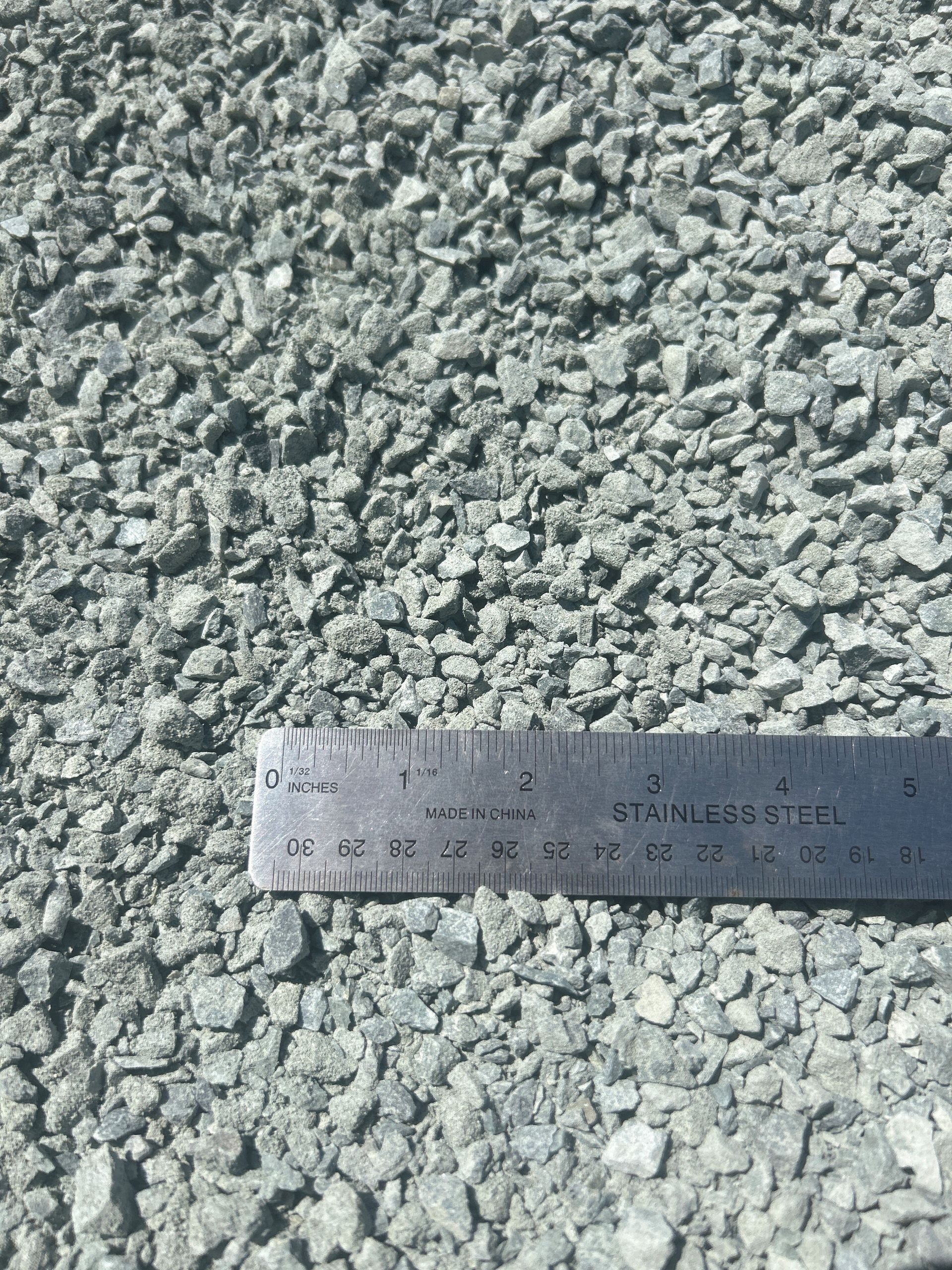 Crushed gravel with a ruler for scale, showing a mix of light gray and blue-gray rock.