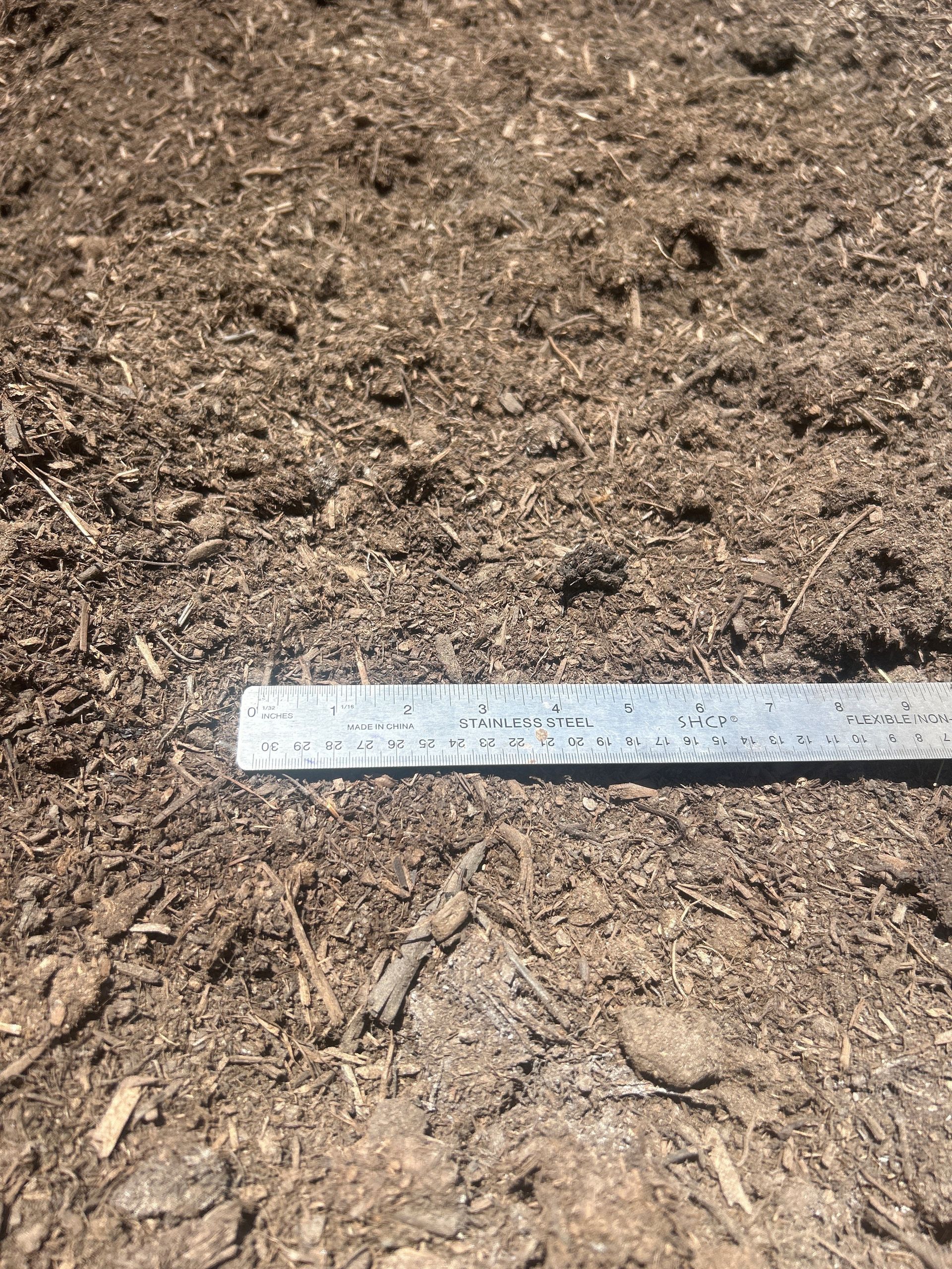 Close-up of brown mulch with a ruler resting on top for scale.