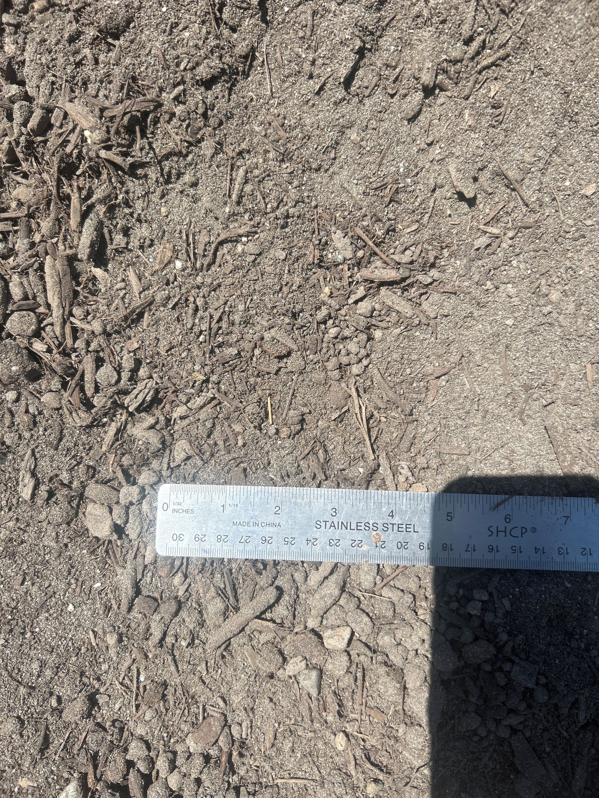 Soil with a metal ruler for scale, showing various-sized particles and organic matter.