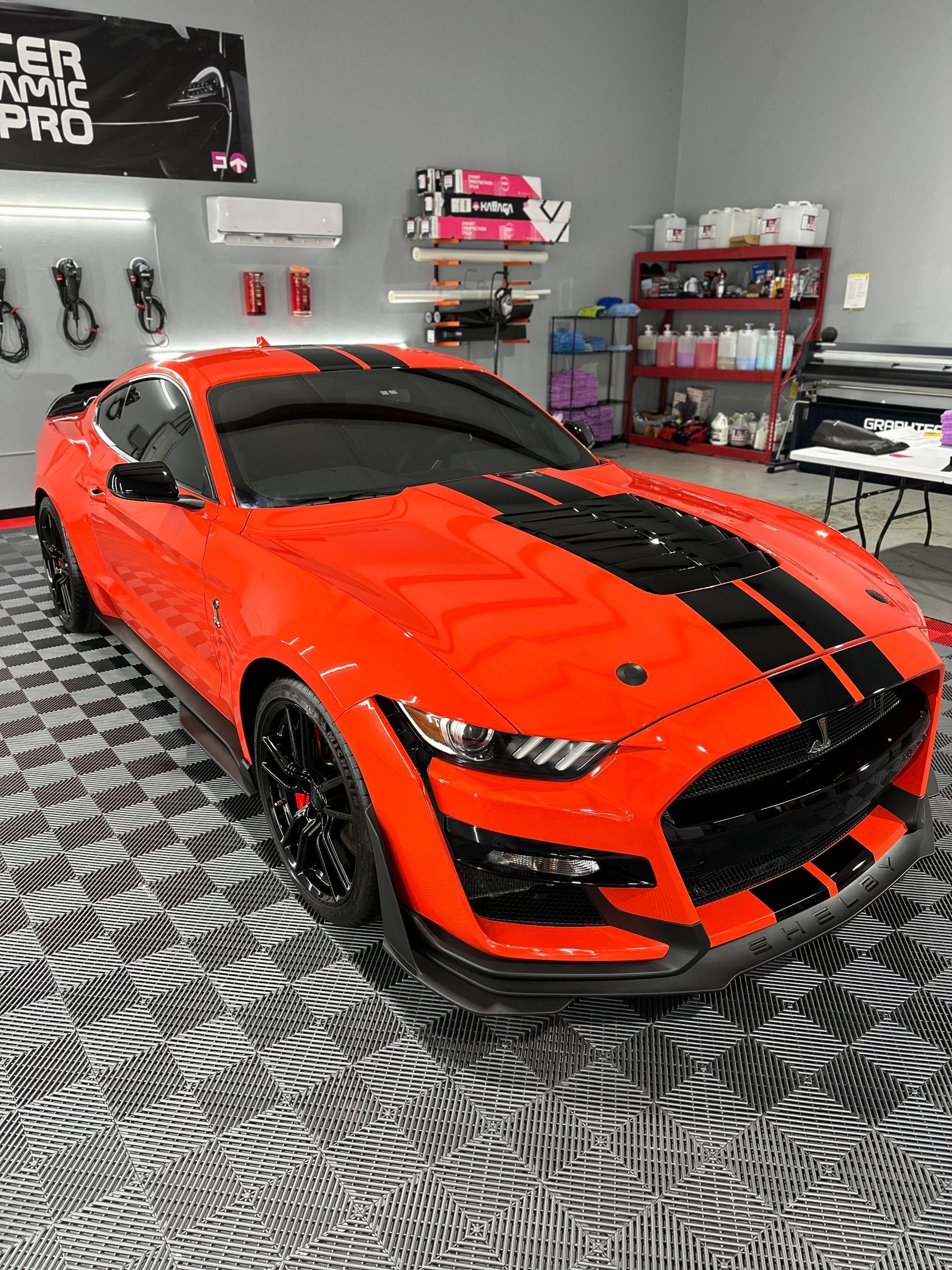 A red mustang with black stripes is parked in a garage.