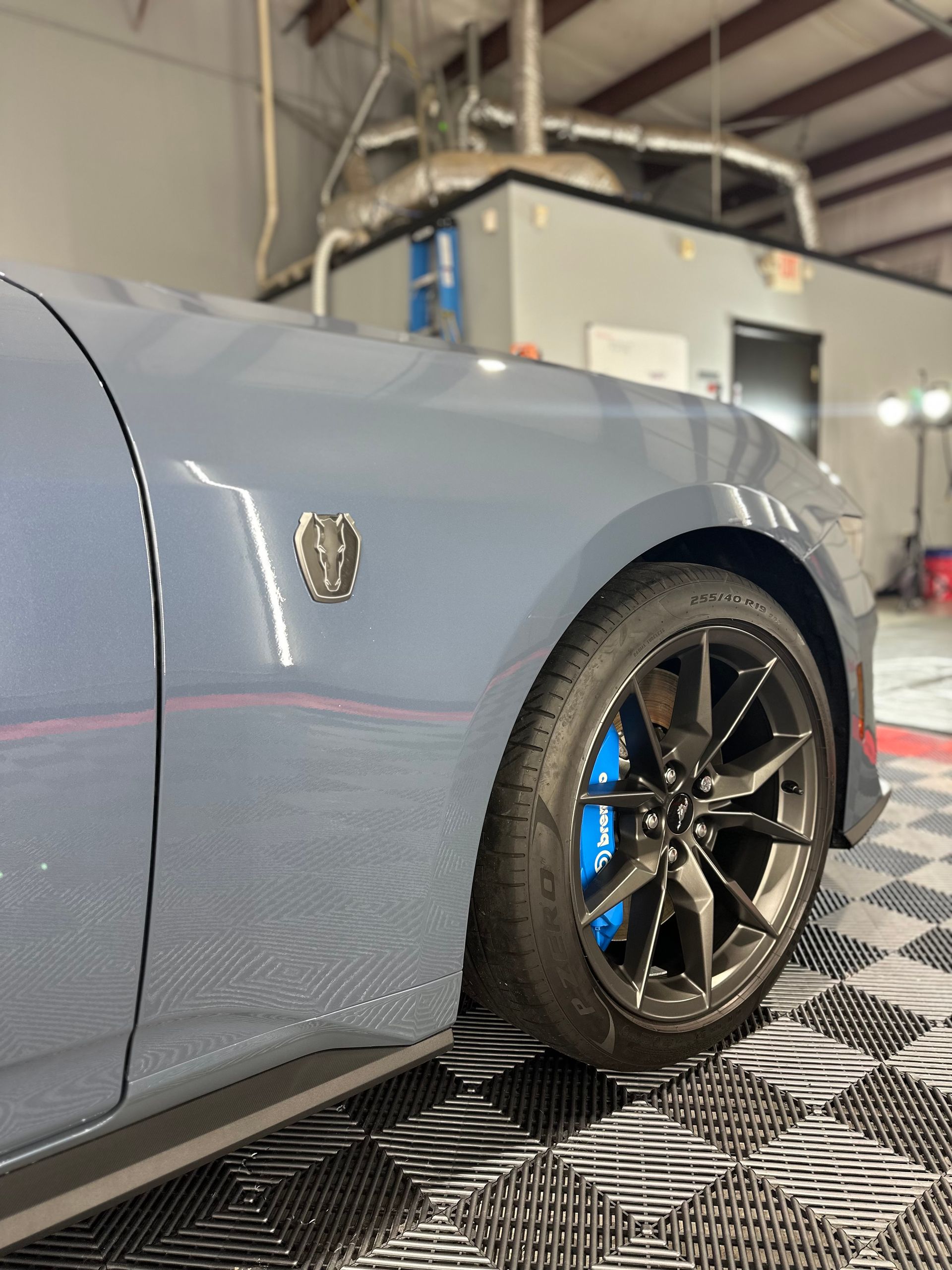 A gray car with blue brake calipers is parked in a garage.