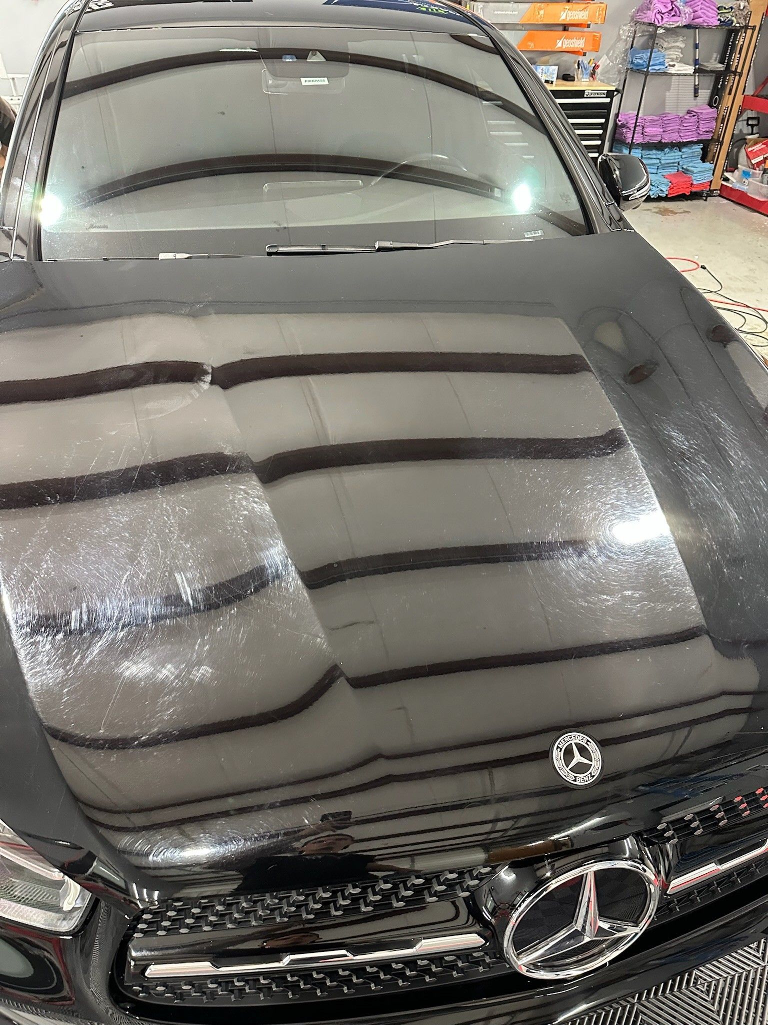 Black Mercedes car hood reflecting overhead lights and display shelves.