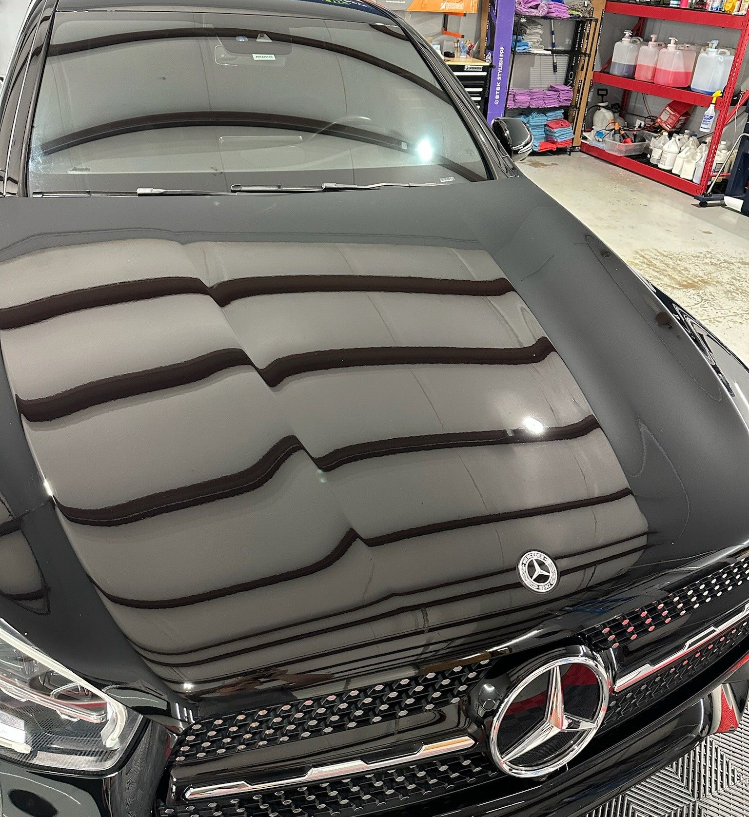 Black Mercedes-Benz hood with reflection of shop interior. Chrome grill and emblem visible.