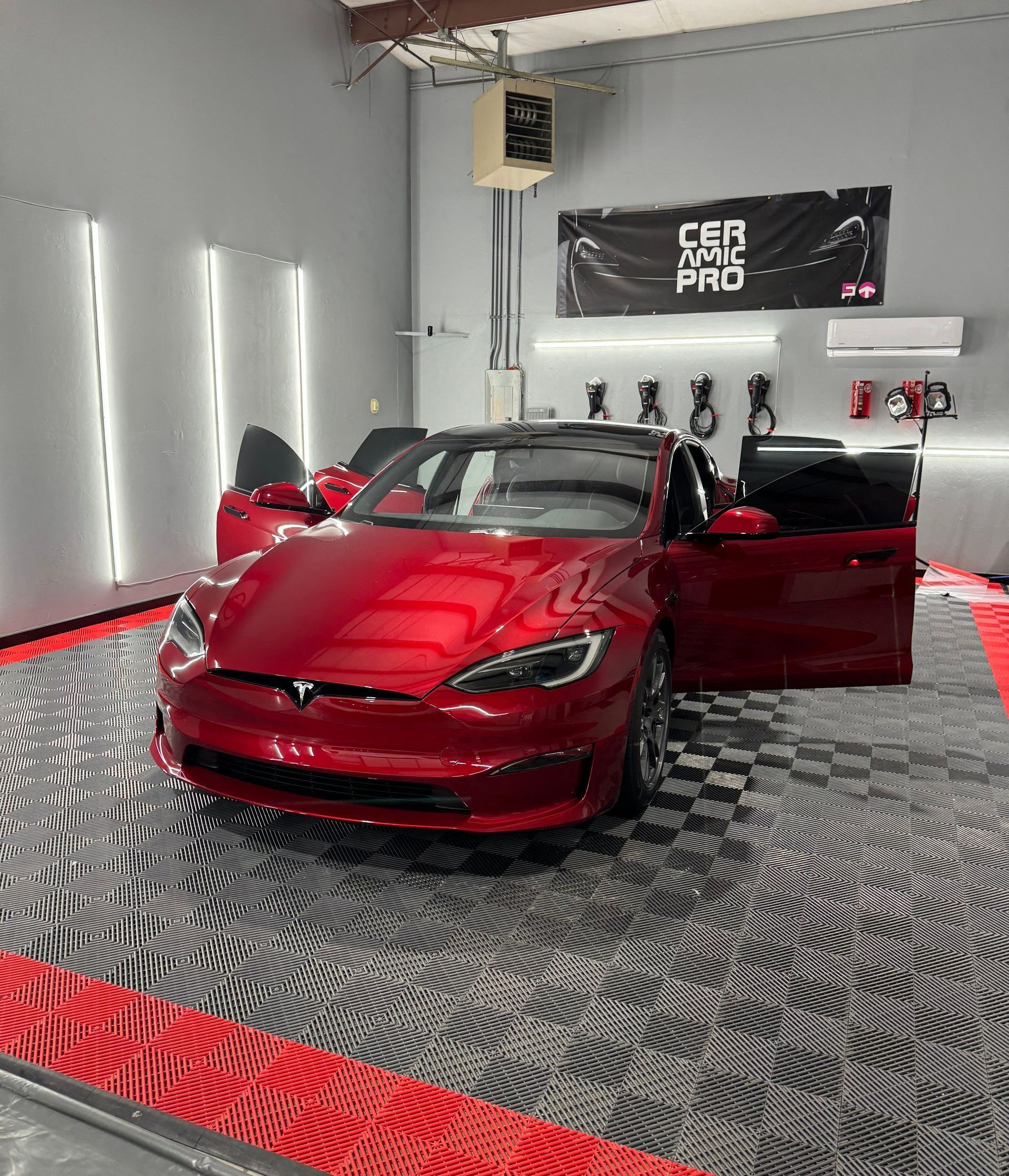 A red tesla model s is parked in a garage with its doors open.