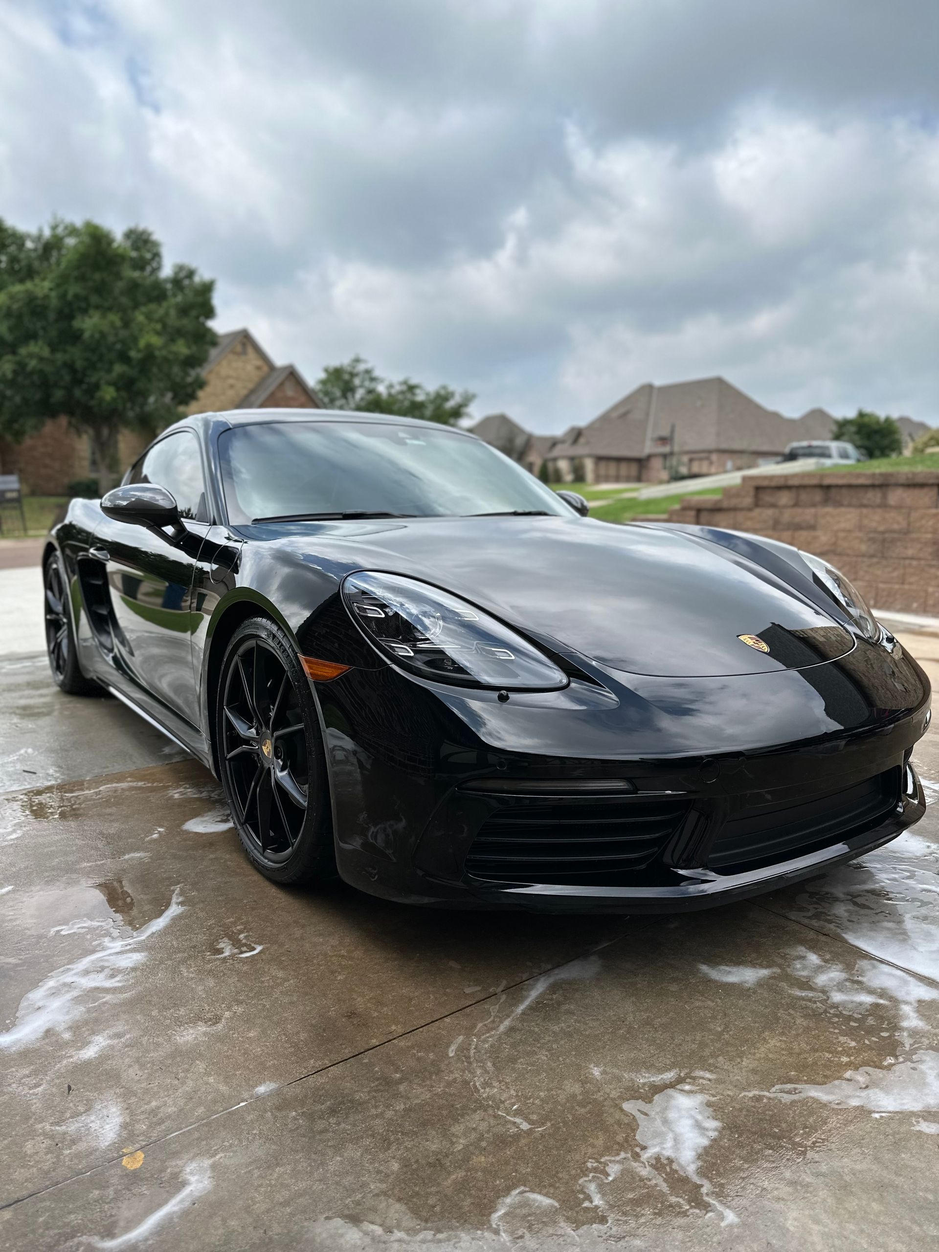 A black sports car is parked in a driveway next to a house.