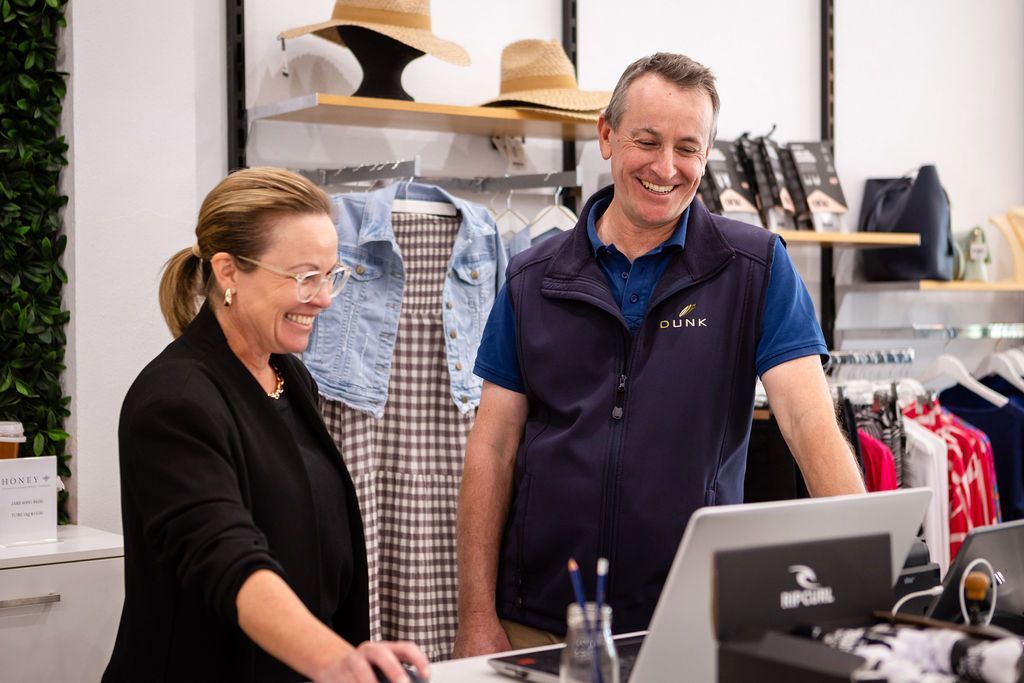 A man and a woman are standing in front of a computer in a clothing store.