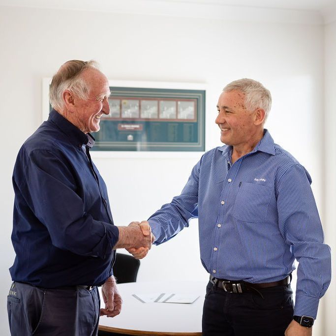 Two men shaking hands in front of a white board