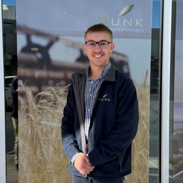 Smiling person in glasses wearing a navy jacket, standing outside a building with a Fünk logo.
