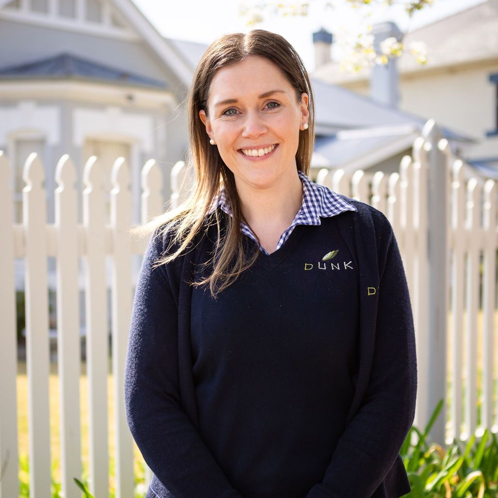 A woman in a blue sweater is standing in front of a white picket fence.