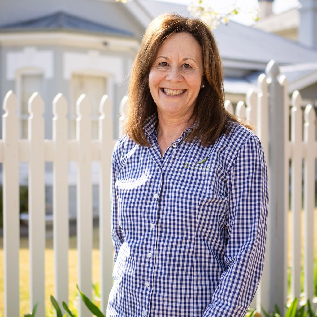 A woman in a plaid shirt is standing in front of a white picket fence.
