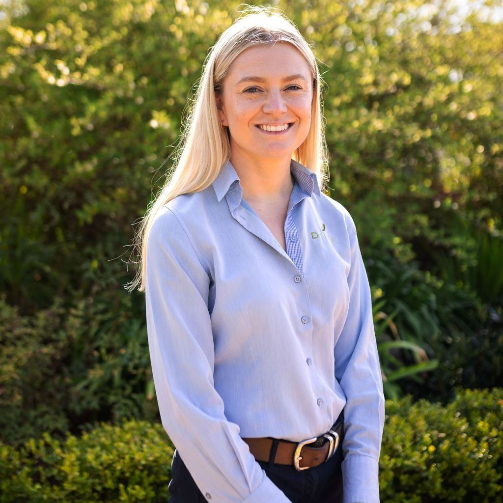 A woman in a blue shirt and brown belt is smiling for the camera.