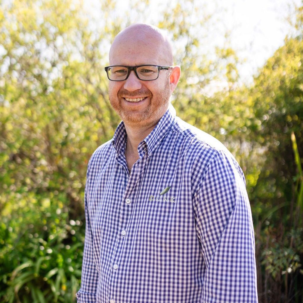 A bald man wearing glasses and a plaid shirt is smiling for the camera.