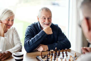 Two older adults smiling over a chessboard during a game at a table